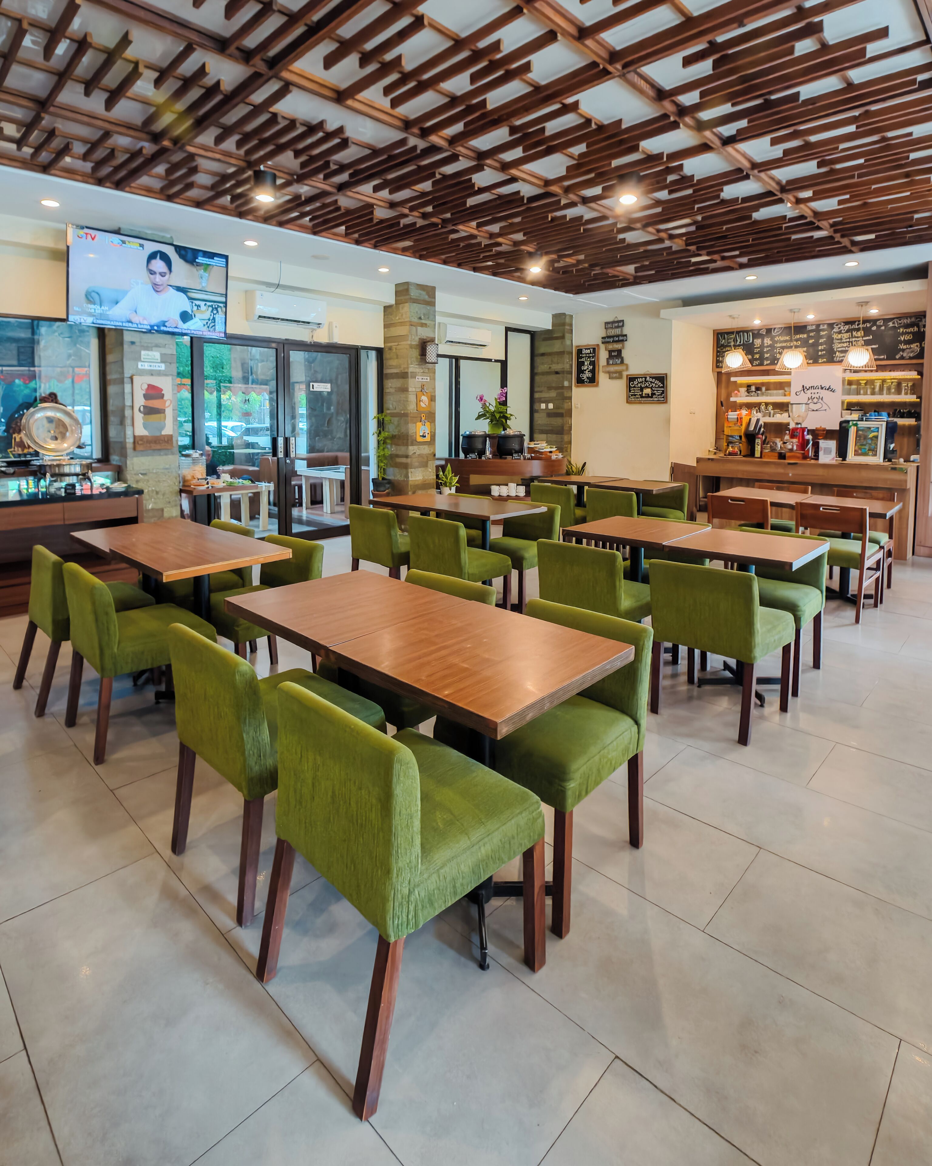 A restaurant interior with wooden tables and green chairs, a bar area, and a TV screen.