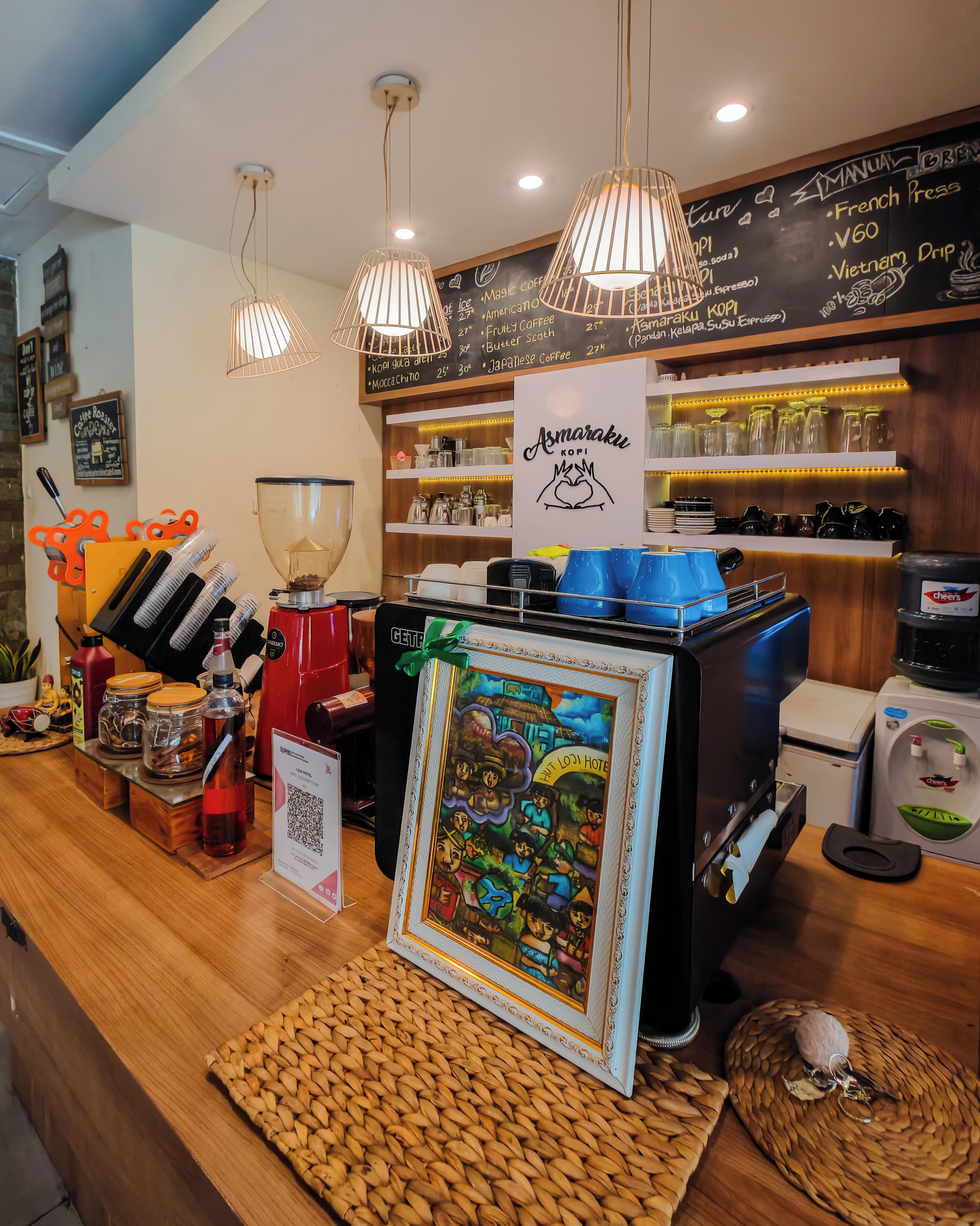 A coffee shop interior with a chalkboard menu, espresso machines, and a framed artwork on the counter.