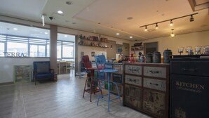 Una habitación amplia con un gran ventanal, un sofá azul, una silla roja y una zona de bar con armarios de estilo vintage.