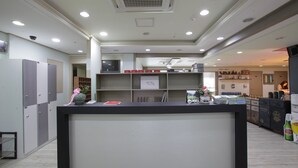 Un área de recepción con mostrador, estantes con cajas rojas y una cocina al fondo.