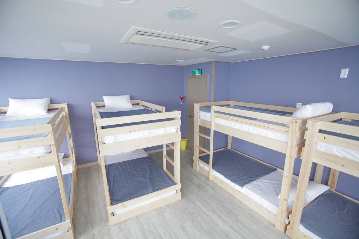 A room with four bunk beds, wooden frames, and blue bedding.