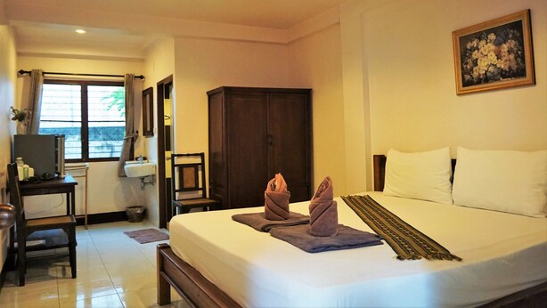 A hotel room with a bed, a desk with a chair, a wardrobe, a painting on the wall, and a window with curtains. - My Mum Home (Chiang Mai)