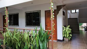 A covered outdoor area with potted plants, a wooden door, and a staircase leading to an upper level. - My Mum Home (Chiang Mai)