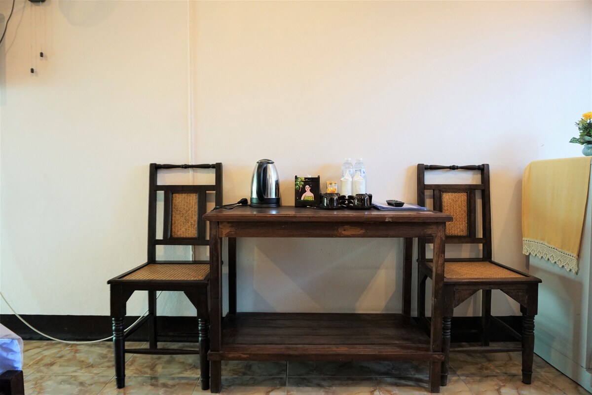 A small wooden table with two chairs, a kettle, and a few bottles on it.
