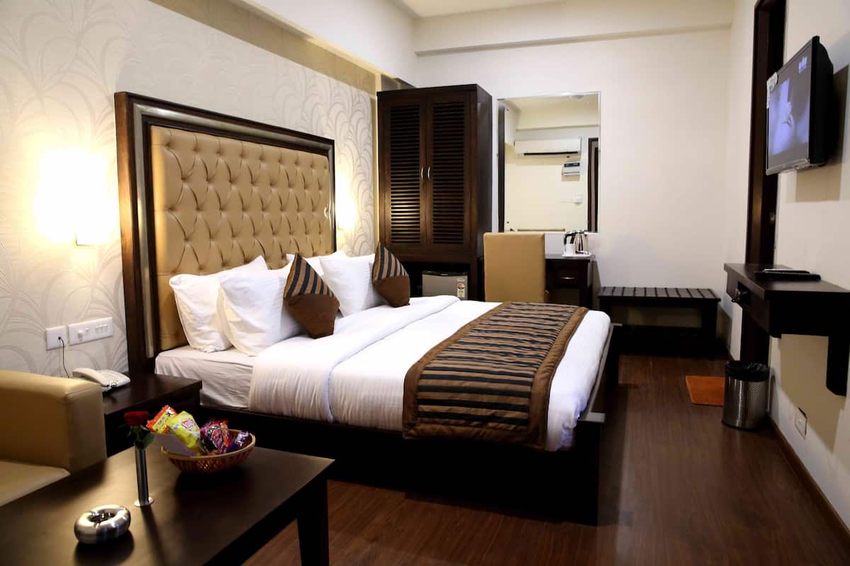 A hotel room with a large bed, a bedside table with a lamp, a TV, and a wardrobe.