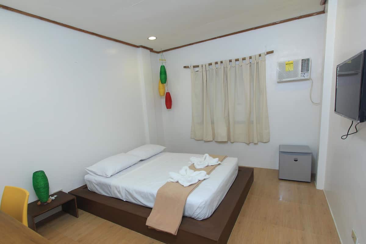 A bedroom with a bed, bedside tables, a TV, an air conditioner, and a small cabinet.