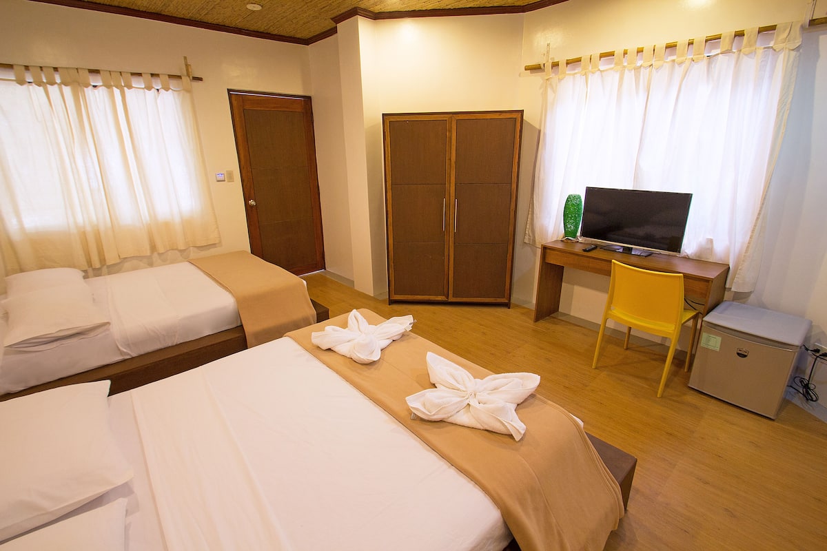 A hotel room with two beds, a wardrobe, a desk with a television, and a small refrigerator.