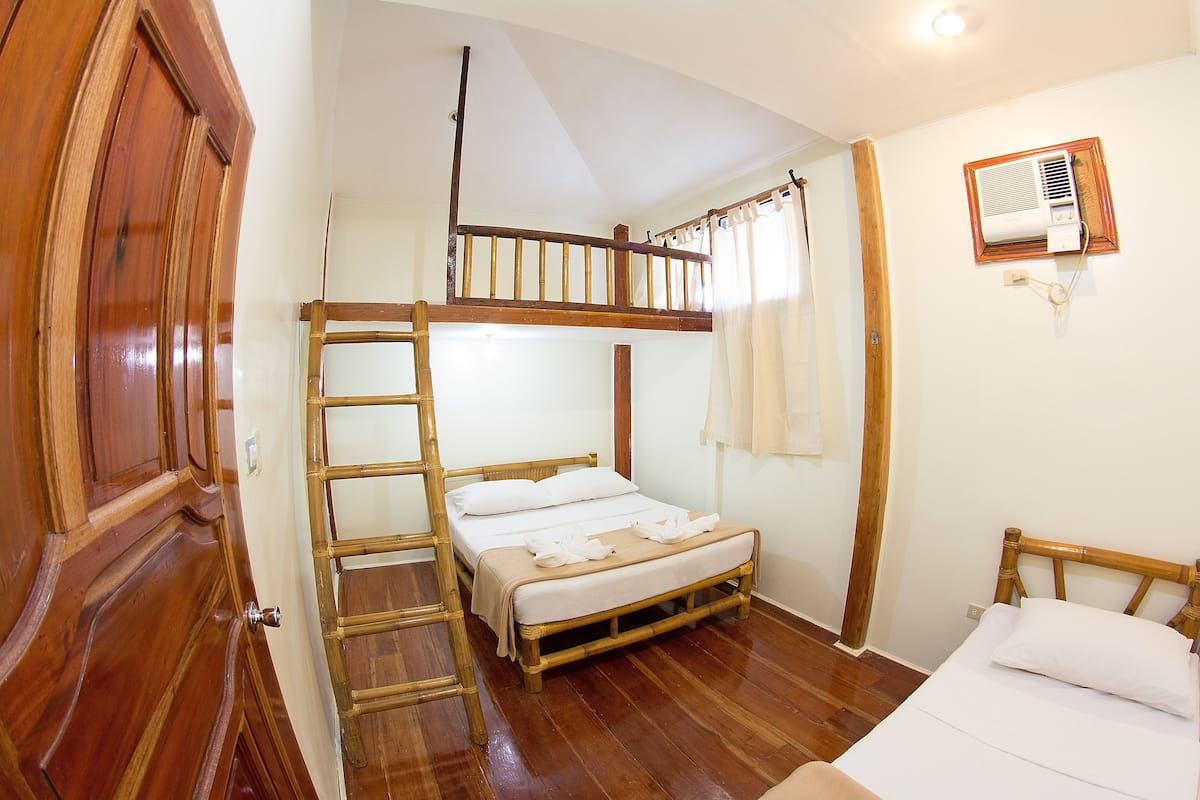 A room with a bunk bed, wooden flooring, a ladder, a wall-mounted air conditioner, and a door with a wooden frame.