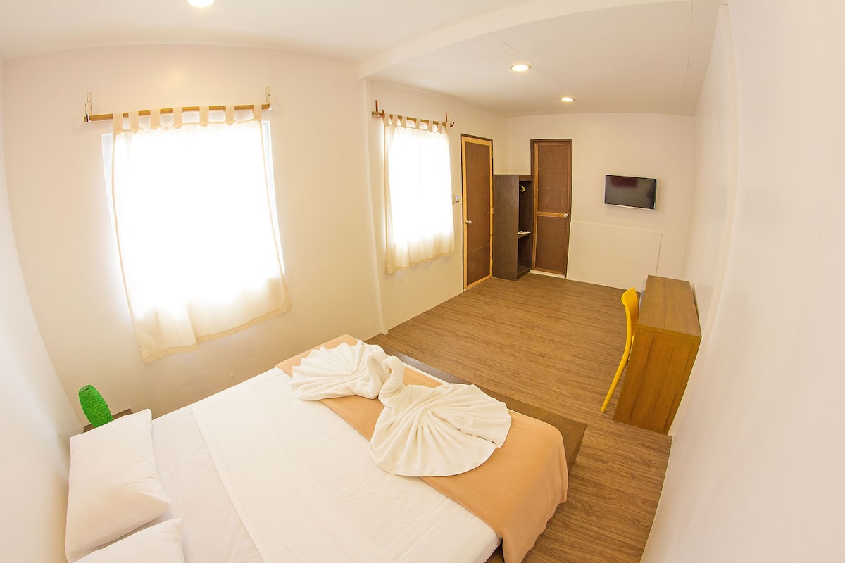 A hotel room with a bed, a desk, a chair, a television, and a door leading to another room.