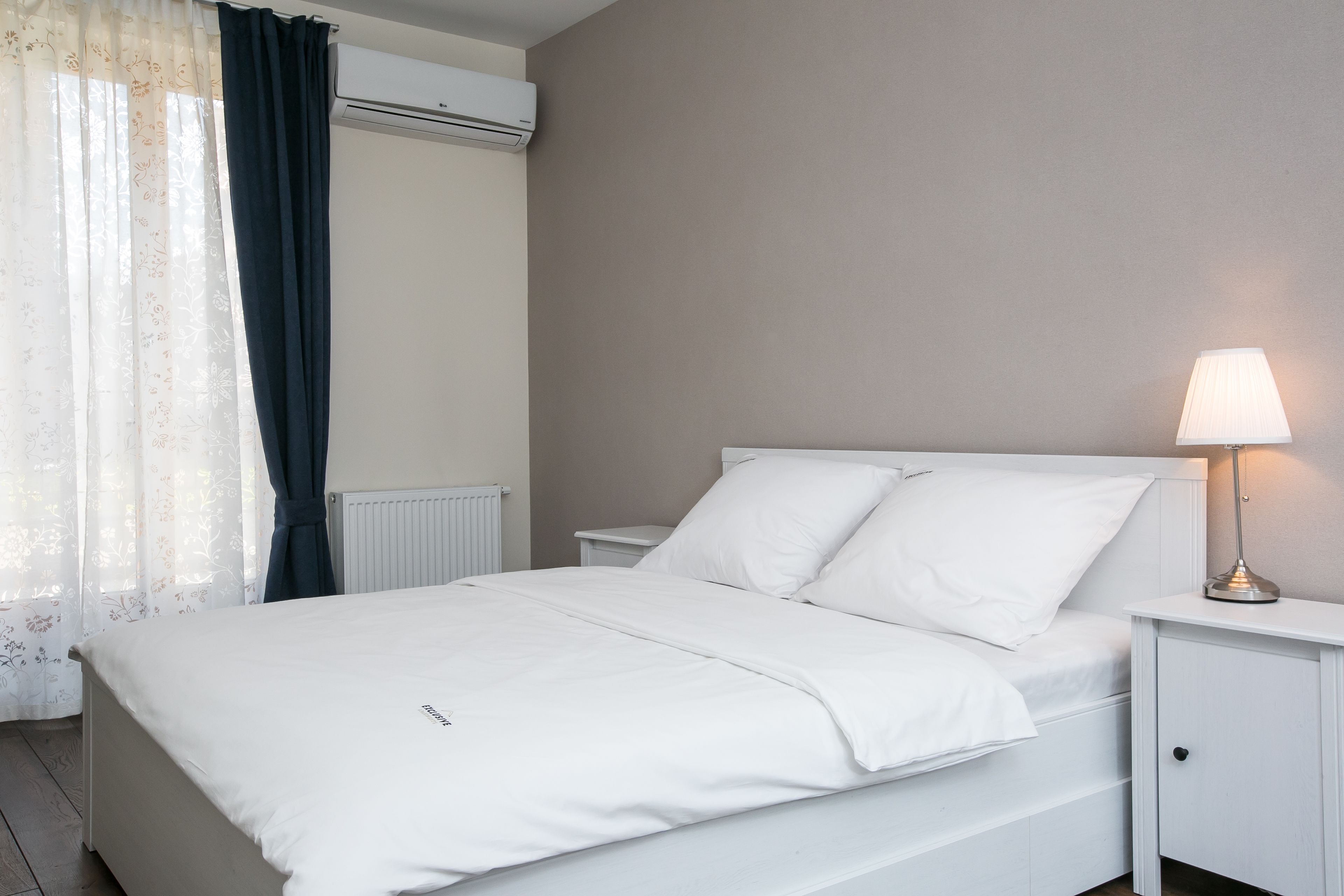 A neatly made bed with white linens, a bedside lamp, and a white nightstand.