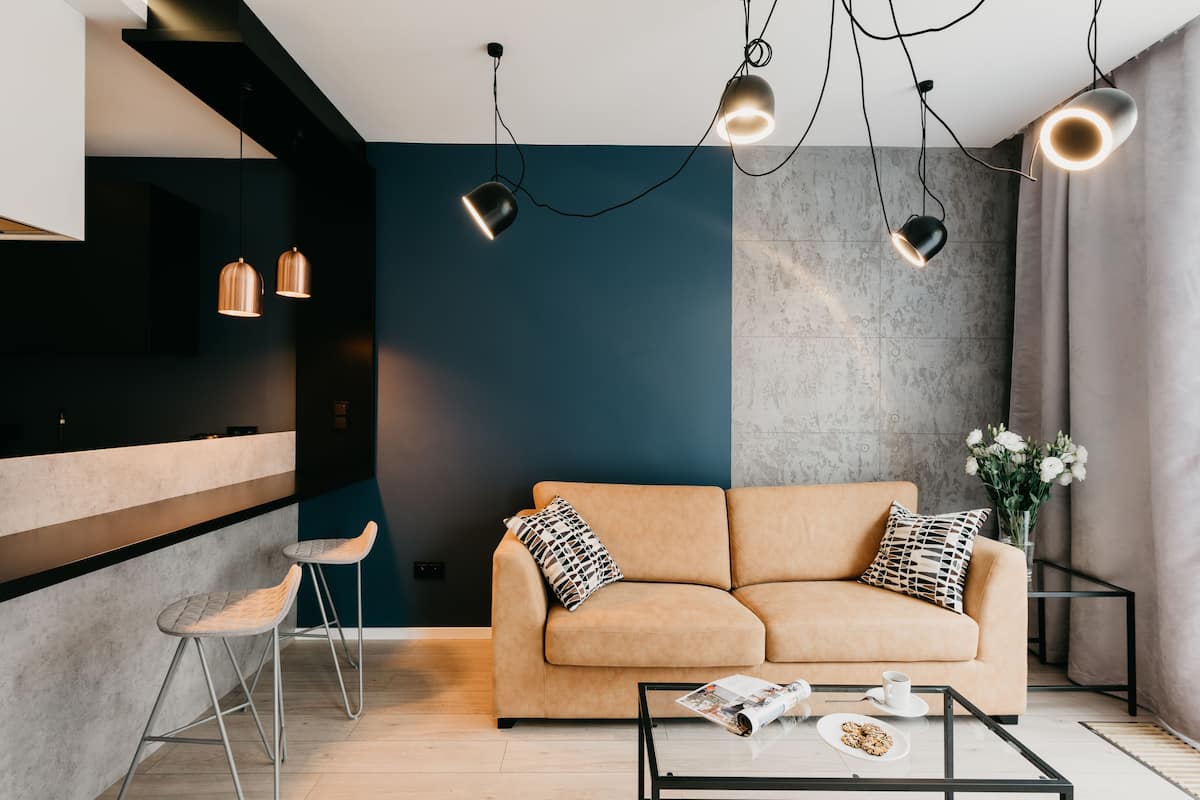 A modern living room with a sofa, two bar stools, a coffee table, and pendant lights.