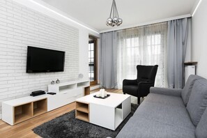 A modern living room with a flat-screen TV mounted on a white brick wall, a grey sofa, a black armchair, and a white coffee table. - Exclusive Apartments | Krakow Lubicz Brewery (Kraków)
