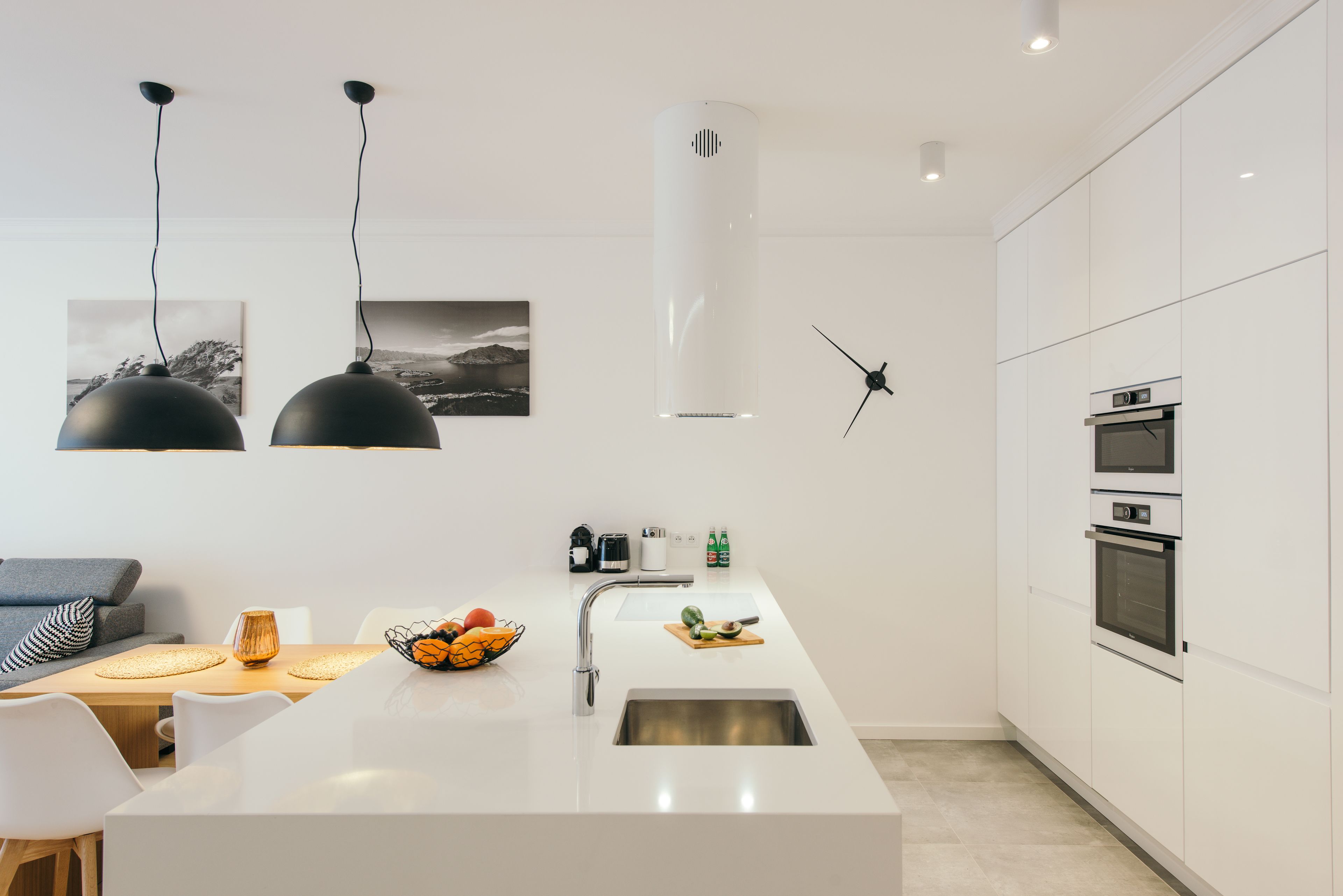 A modern kitchen with a central island, white cabinetry, a built-in oven, and pendant lighting.
