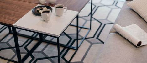 A modern living room with a geometric patterned rug, a wooden coffee table with a white mug and teapot, and a beige sofa with a rolled-up magazine.