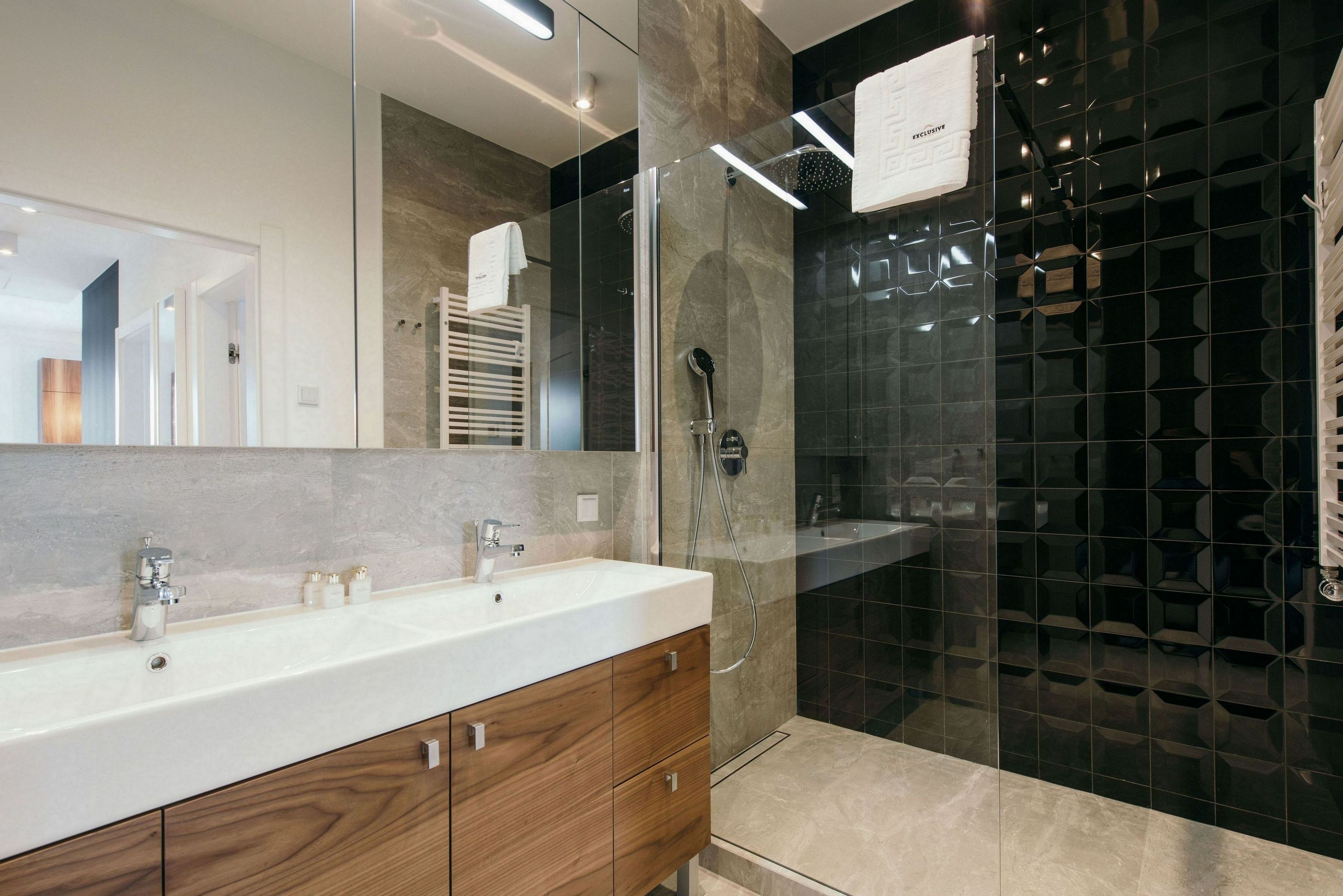 Un baño moderno con un espejo grande, un lavabo blanco, armarios de madera y una zona de ducha con mampara de vidrio.