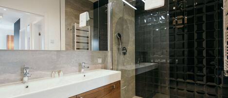 Un baño moderno con un espejo grande, un lavabo blanco, armarios de madera y una zona de ducha con mampara de vidrio.