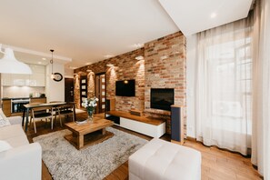Un soggiorno moderno con parete in mattoni, televisione a schermo piatto, tavolino in legno e divano bianco.