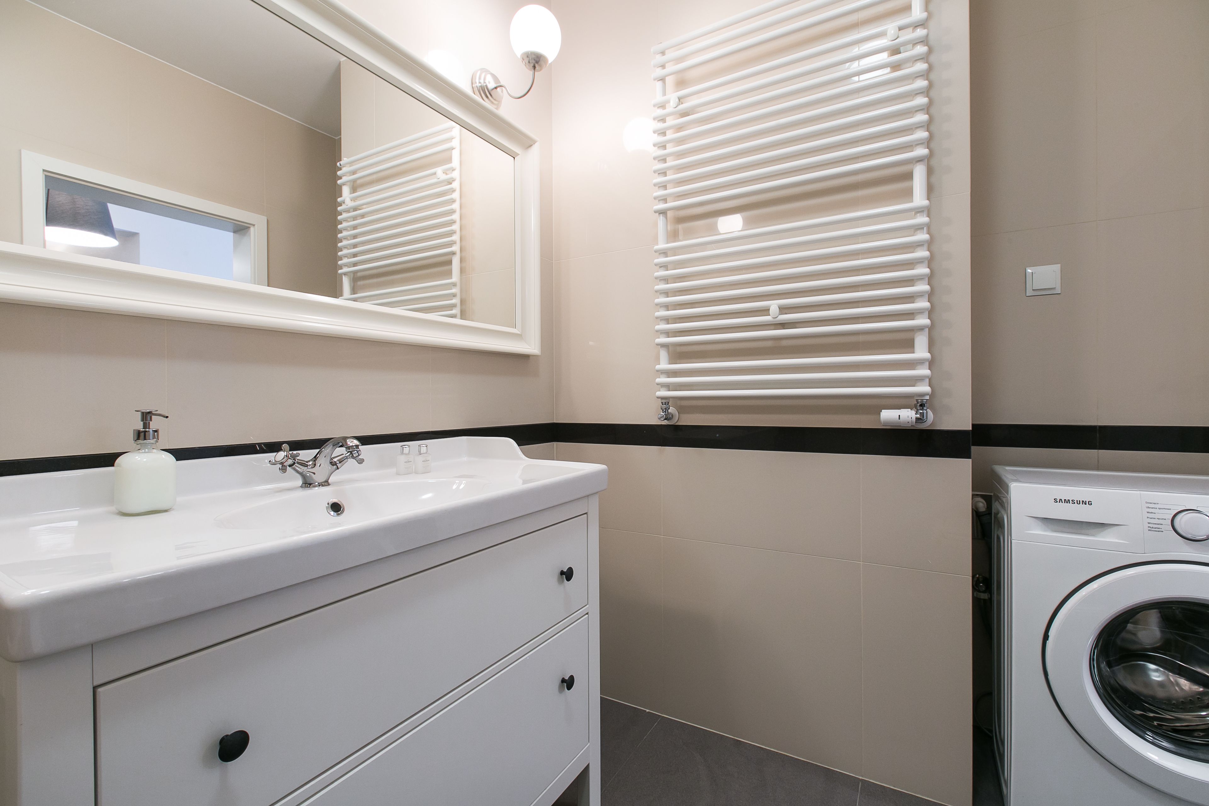 Casa de banho com lavatório branco, espelho, aquecedor fixado na parede e máquina de lavar roupa Samsung.