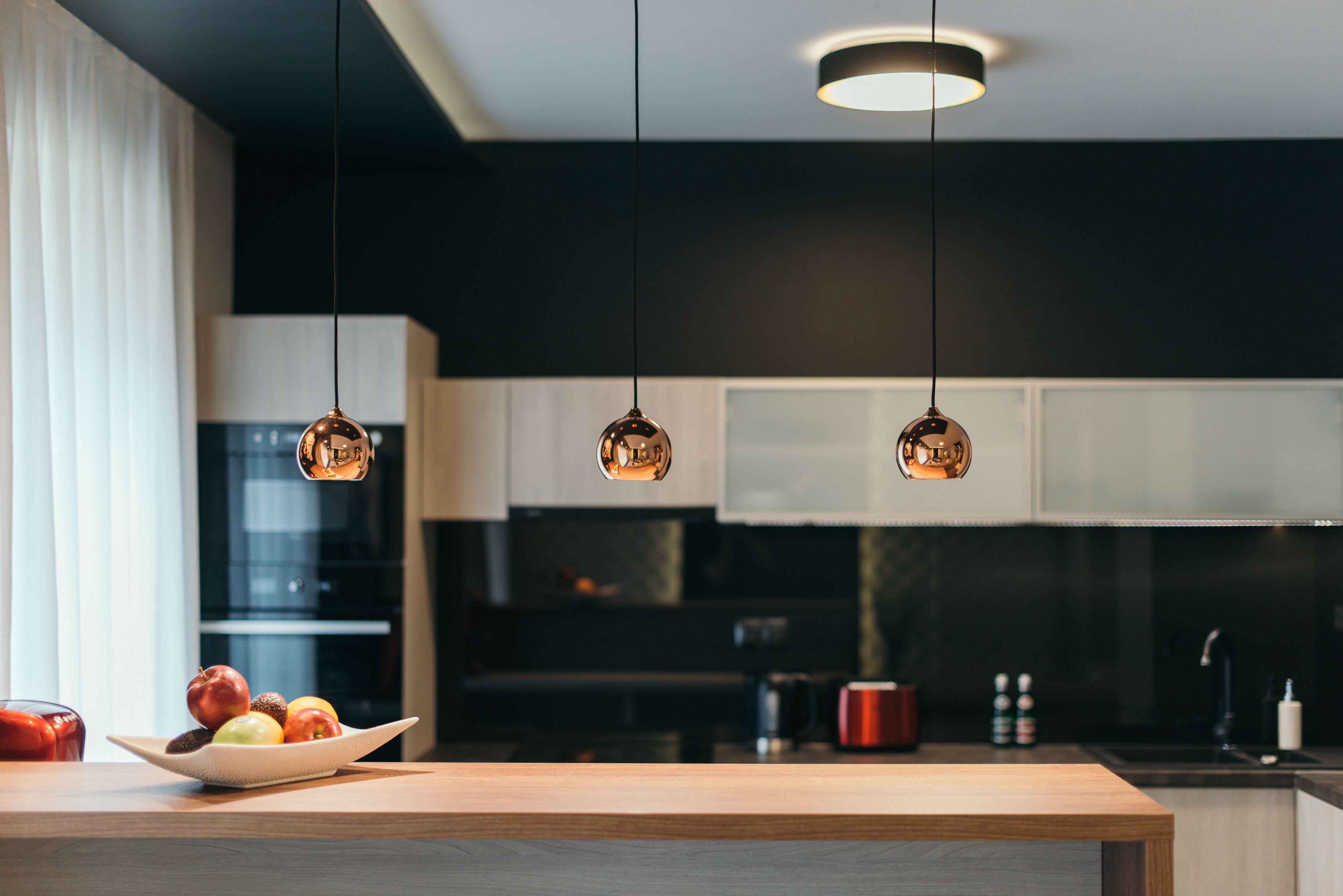 A modern kitchen with pendant lights, a wooden countertop, and a bowl of fruit.