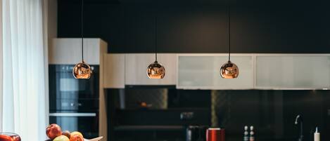 A modern kitchen with pendant lights, a wooden countertop, and a bowl of fruit.