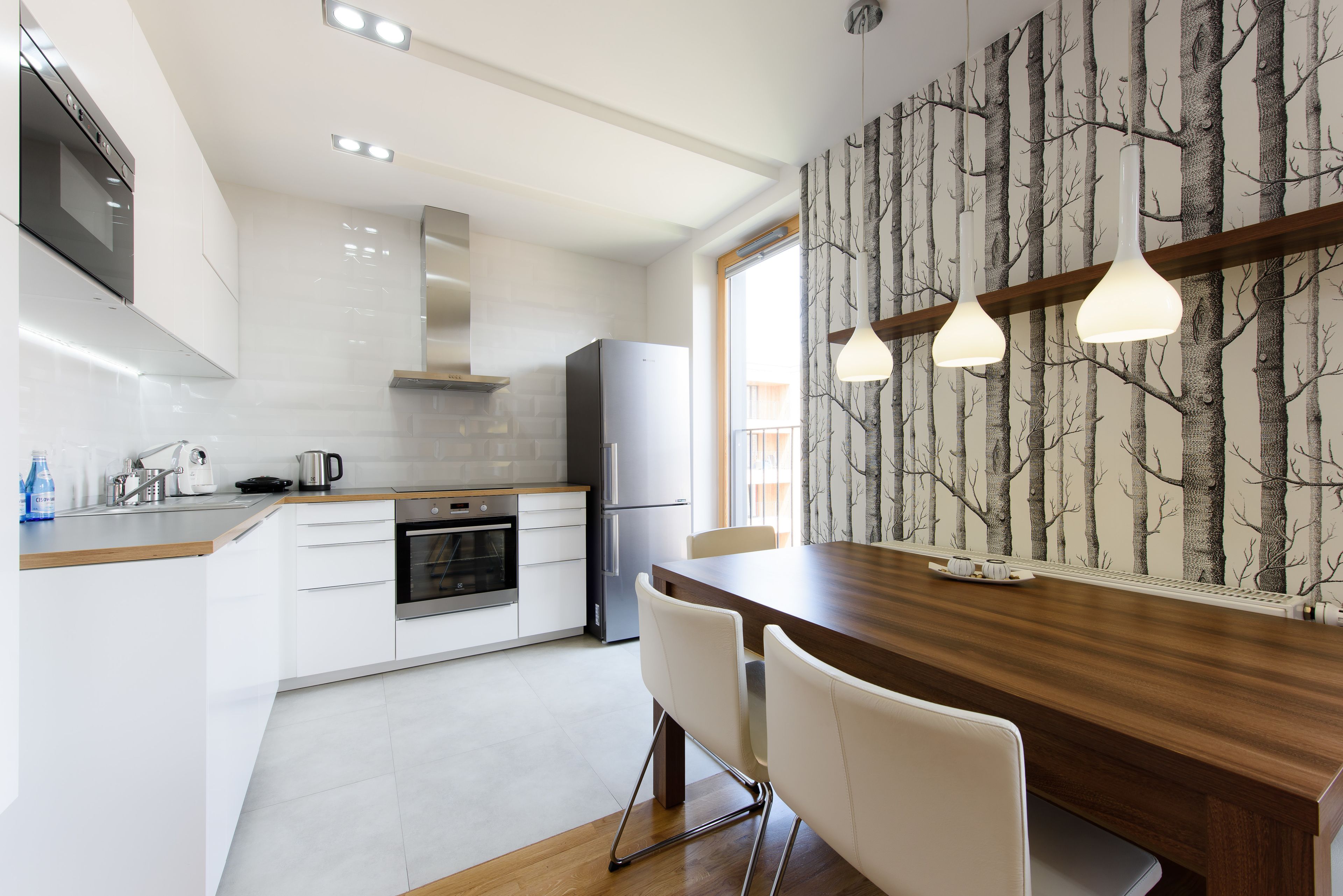 Eine moderne Küche mit weißen Schränken, einer Holz Arbeitsplatte und einem Essbereich mit Holztisch und weißen Stühlen.