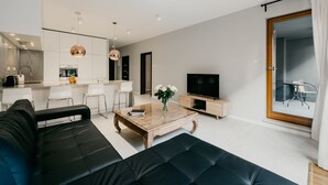 A modern living room with a black leather sofa, a wooden coffee table, and a TV. - Exclusive Apartments | Krakow Lubicz Brewery (Kraków)