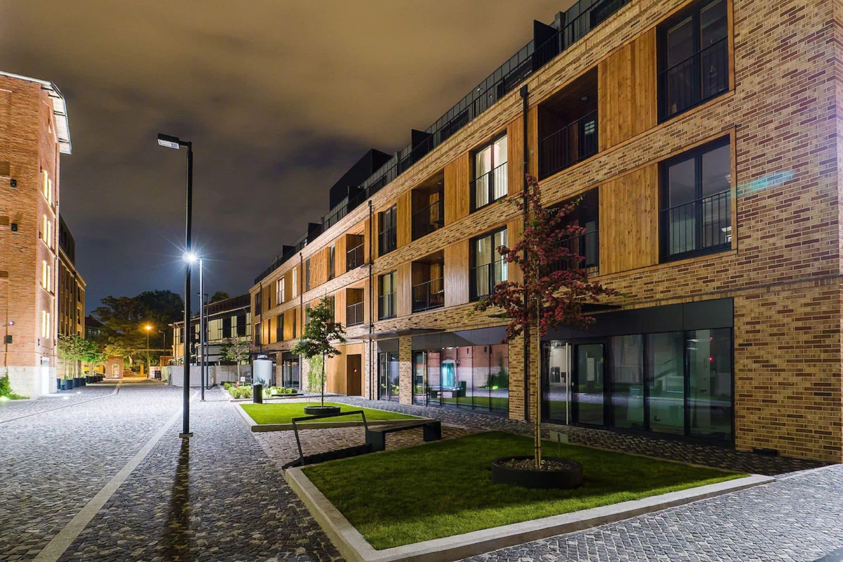A modern building with a brick facade, large windows, and a well-lit courtyard with a small tree and benches.