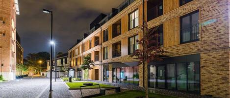 A modern building with a brick facade, large windows, and a well-lit courtyard with a small tree and benches.