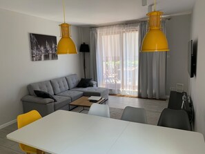 A modern living room with a grey sectional sofa, a white dining table, and yellow pendant lights. - Exclusive Apartments | Krakow Lubicz Brewery (Kraków)