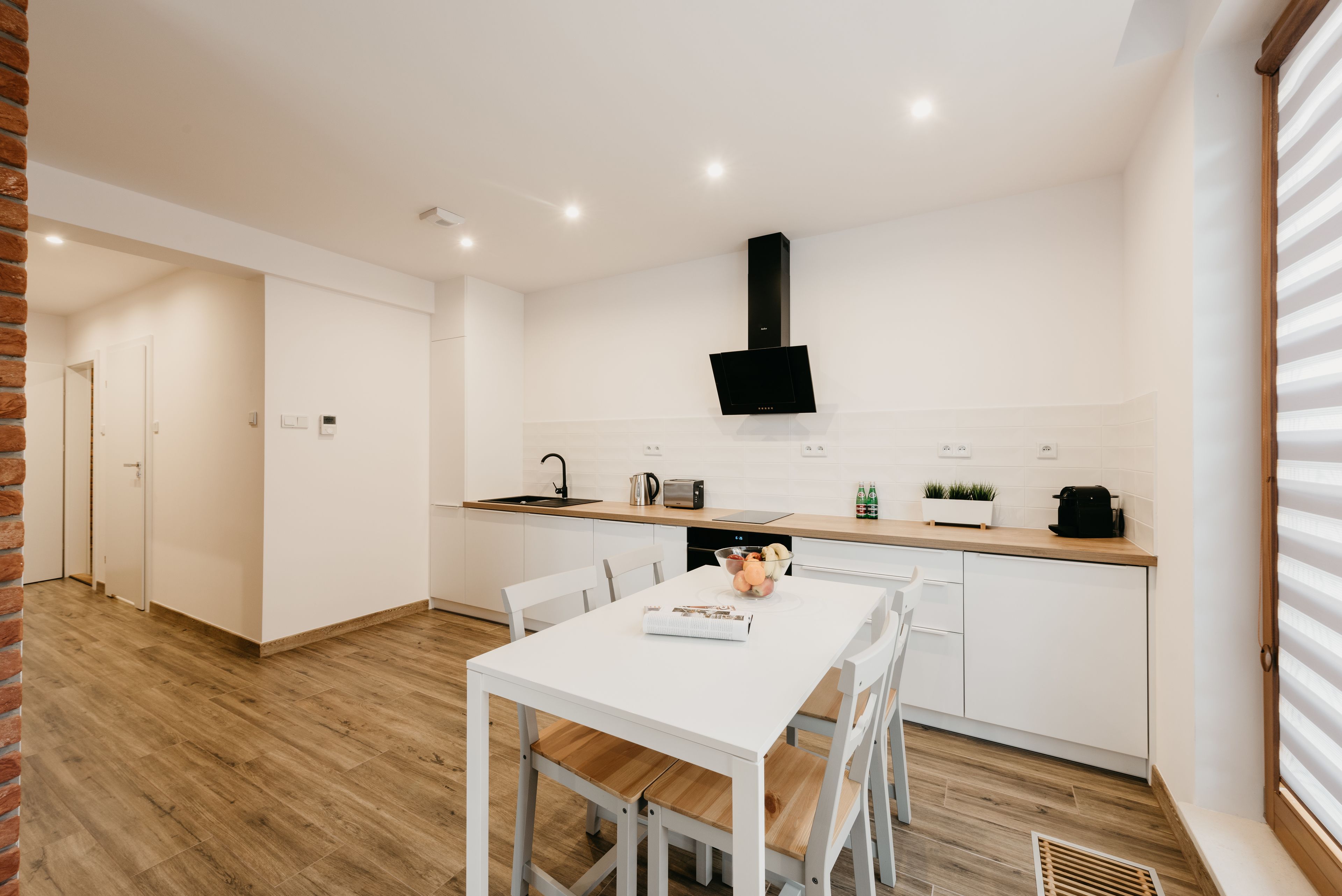A modern kitchen with white cabinetry, a black range hood, and a wooden dining table with chairs.