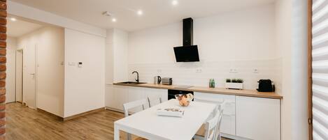 A modern kitchen with white cabinetry, a black range hood, and a wooden dining table with chairs.