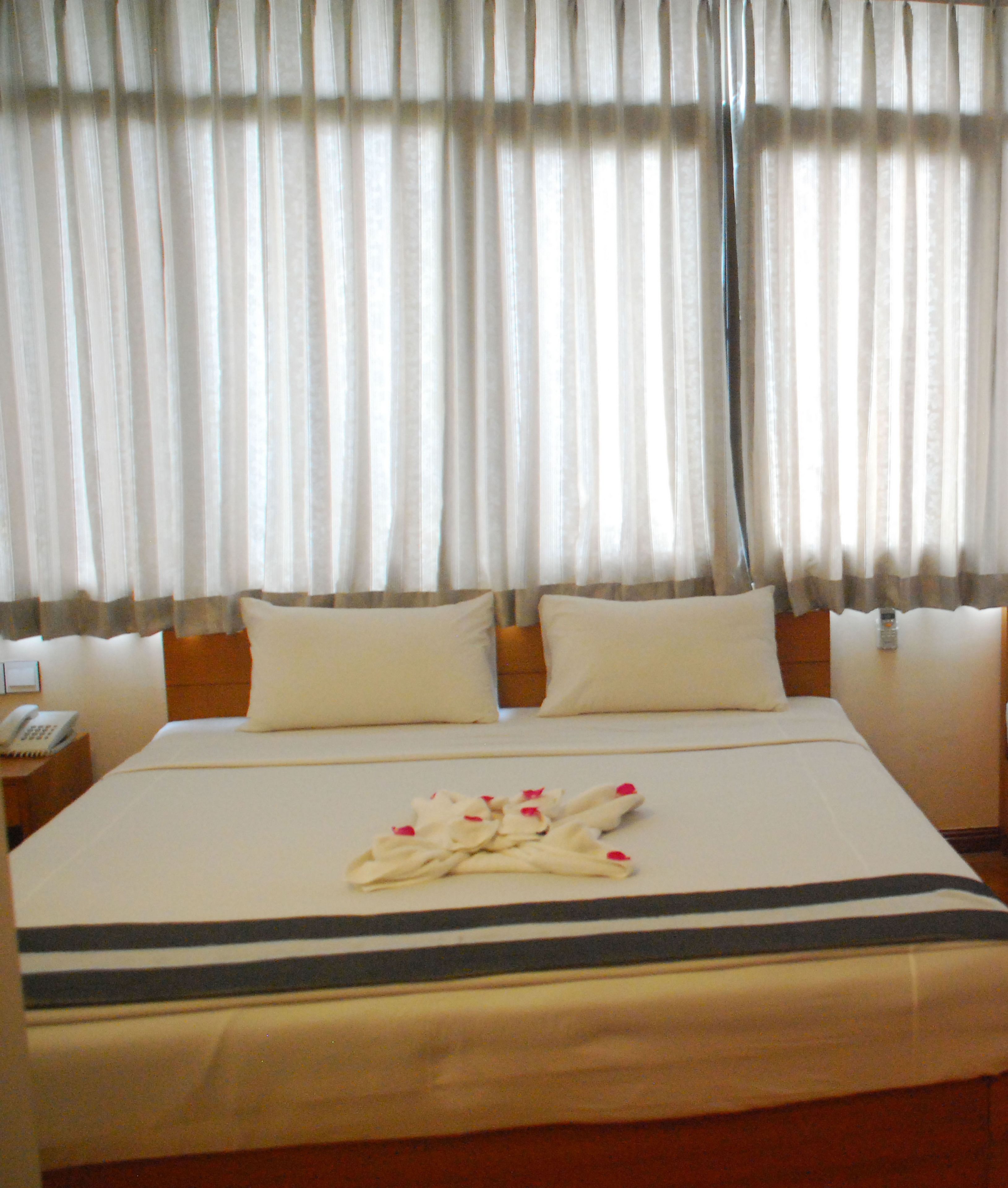 Une chambre d’hôtel avec un grand lit, deux oreillers, une table de chevet avec un téléphone et des rideaux en voile.