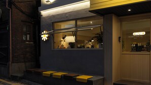 Une entrée d’hôtel moderne avec une façade en verre, un comptoir de réception bien visible et un escalier menant à l’entrée.