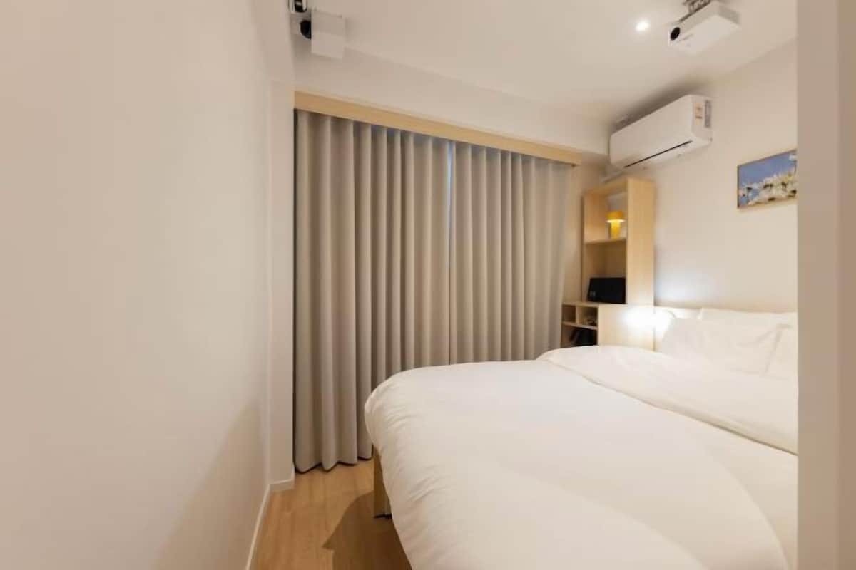 A hotel room with a large bed, a desk with a chair, a wardrobe, and a window with curtains.