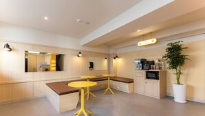 Une cuisine moderne avec des meubles en bois, un four à micro-ondes encastré et une machine à café. On y trouve deux tables jaunes et un banc.