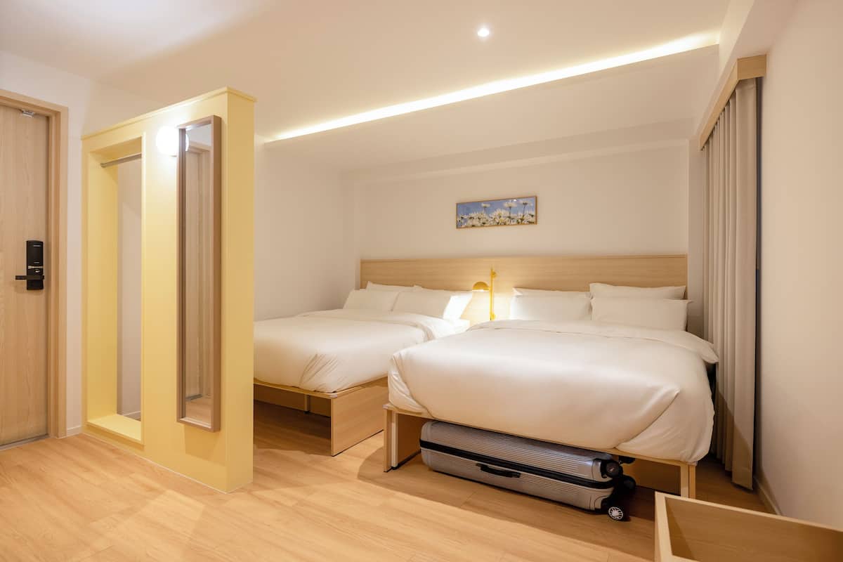 Une chambre d’hôtel avec deux lits, une tête de lit en bois, une lampe de chevet, une valise et un tableau accroché au mur.