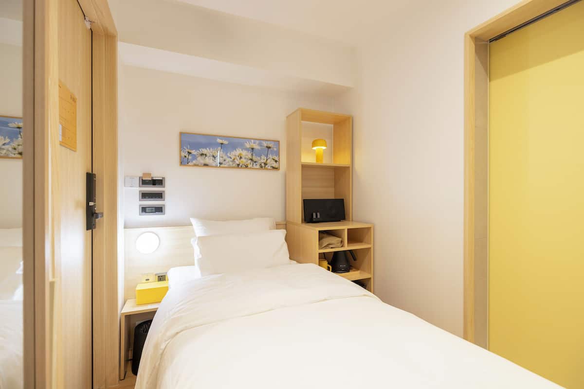 Une chambre d’hôtel avec un lit, un bureau avec une lampe, une étagère avec une lampe et un tableau au mur.