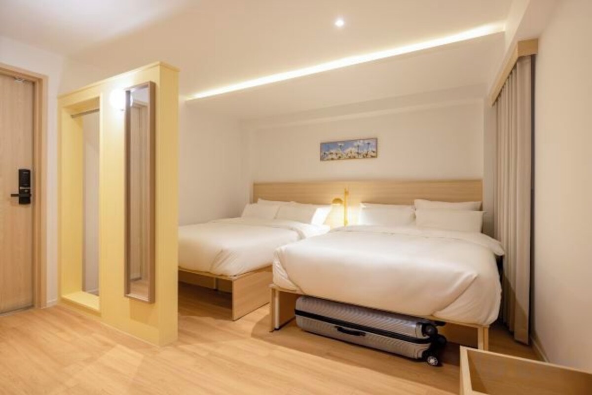 A hotel room with two beds, a wooden floor, a painting on the wall, and a suitcase on the floor.