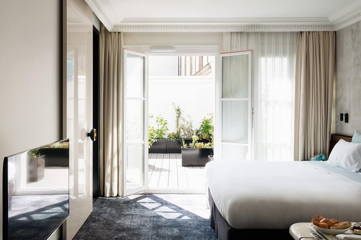 Habitación de hotel con una cama grande, televisión, escritorio y vista al jardín exterior.