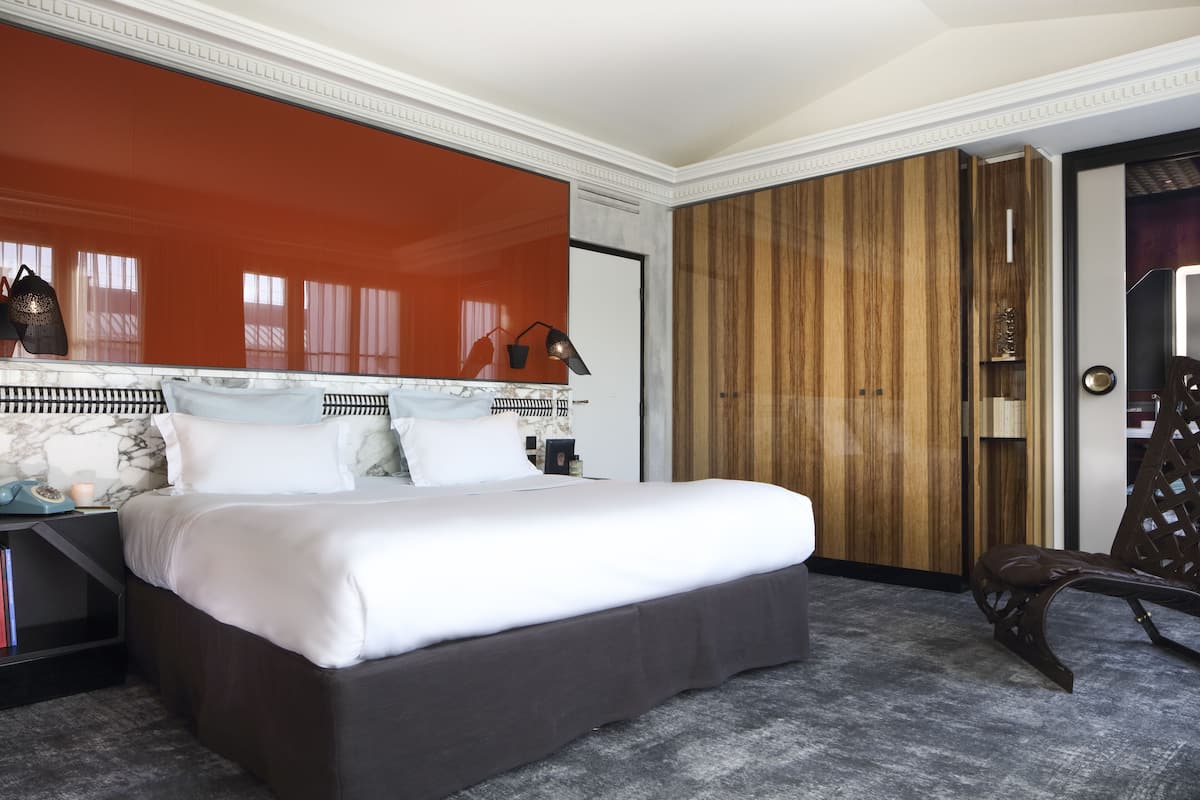 Una habitación de hotel moderna con una cama grande, un armario de madera y una zona de estar con una silla.