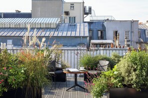 Una terraza en la azotea con mesa y sillas, rodeada de plantas y vistas a la ciudad.