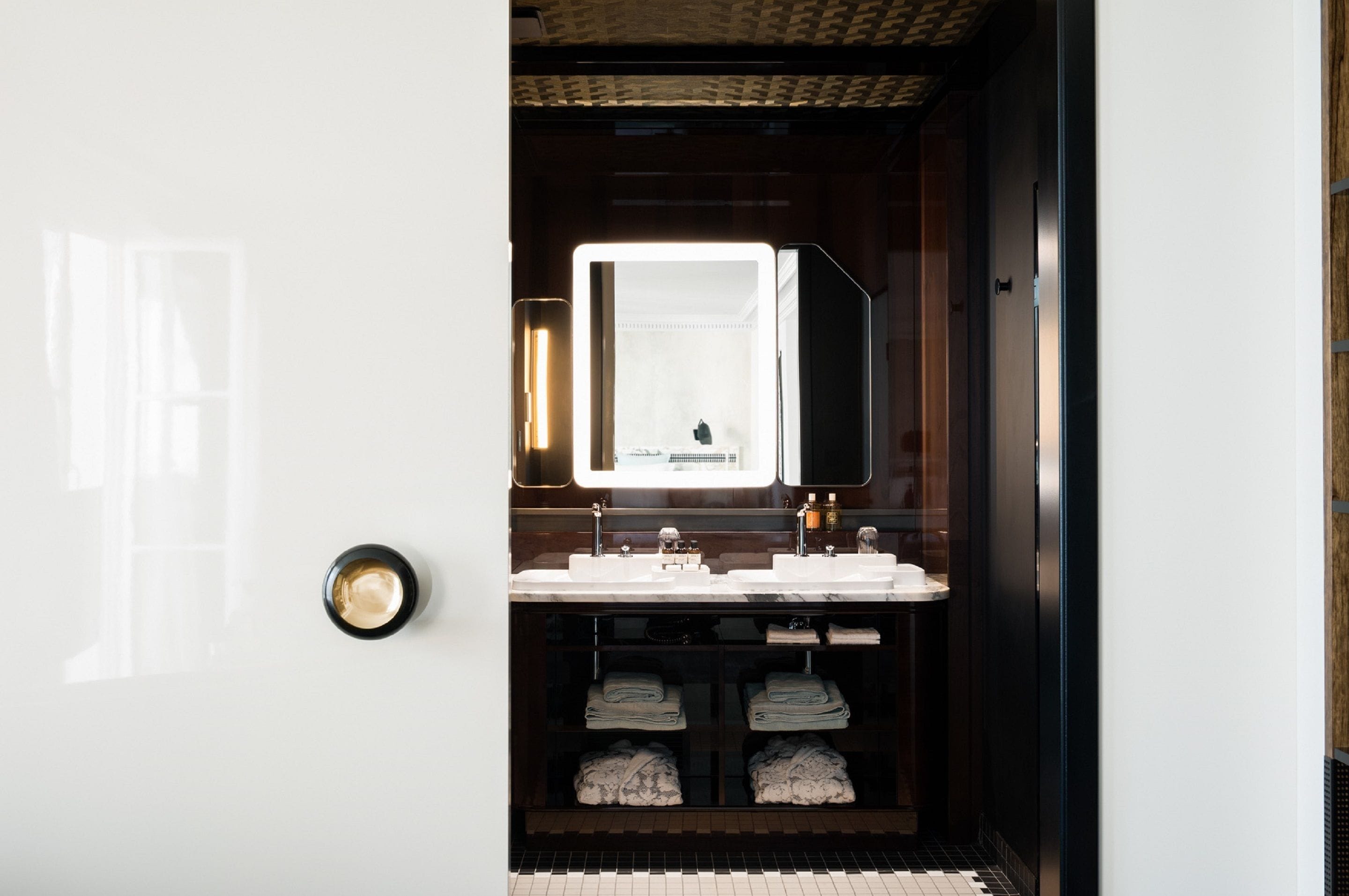 A modern bathroom with a large mirror, dual sinks, and neatly folded towels on shelves.