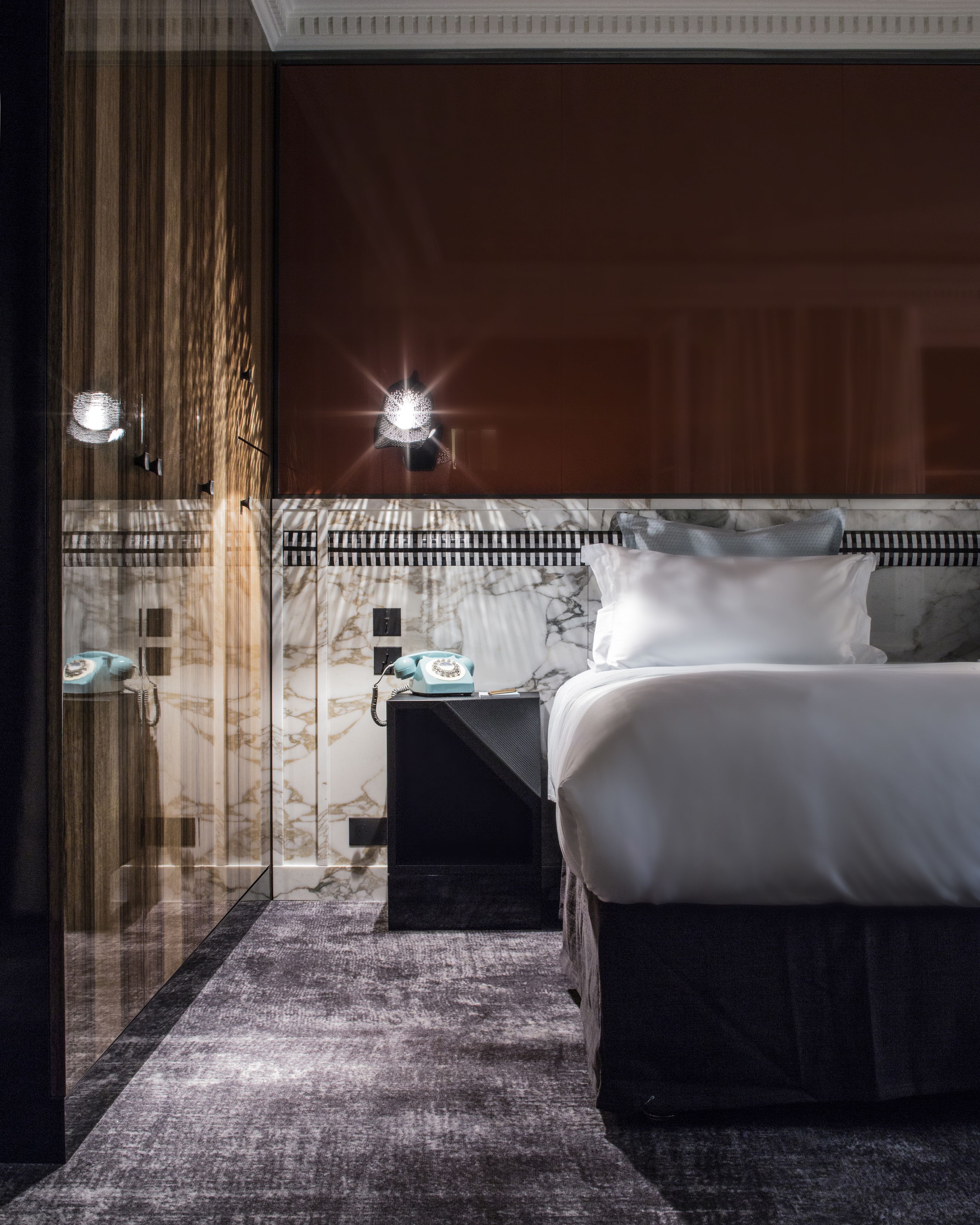 A modern bedroom with a large bed, a nightstand, a glass partition, and a marble wall.