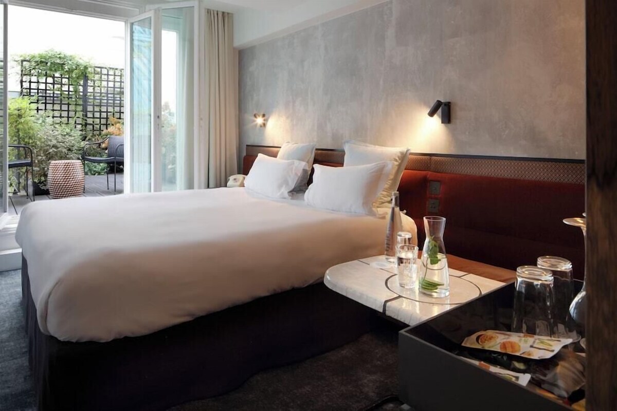 A hotel room with a large bed, a small table with a glass, a bottle, and a menu.