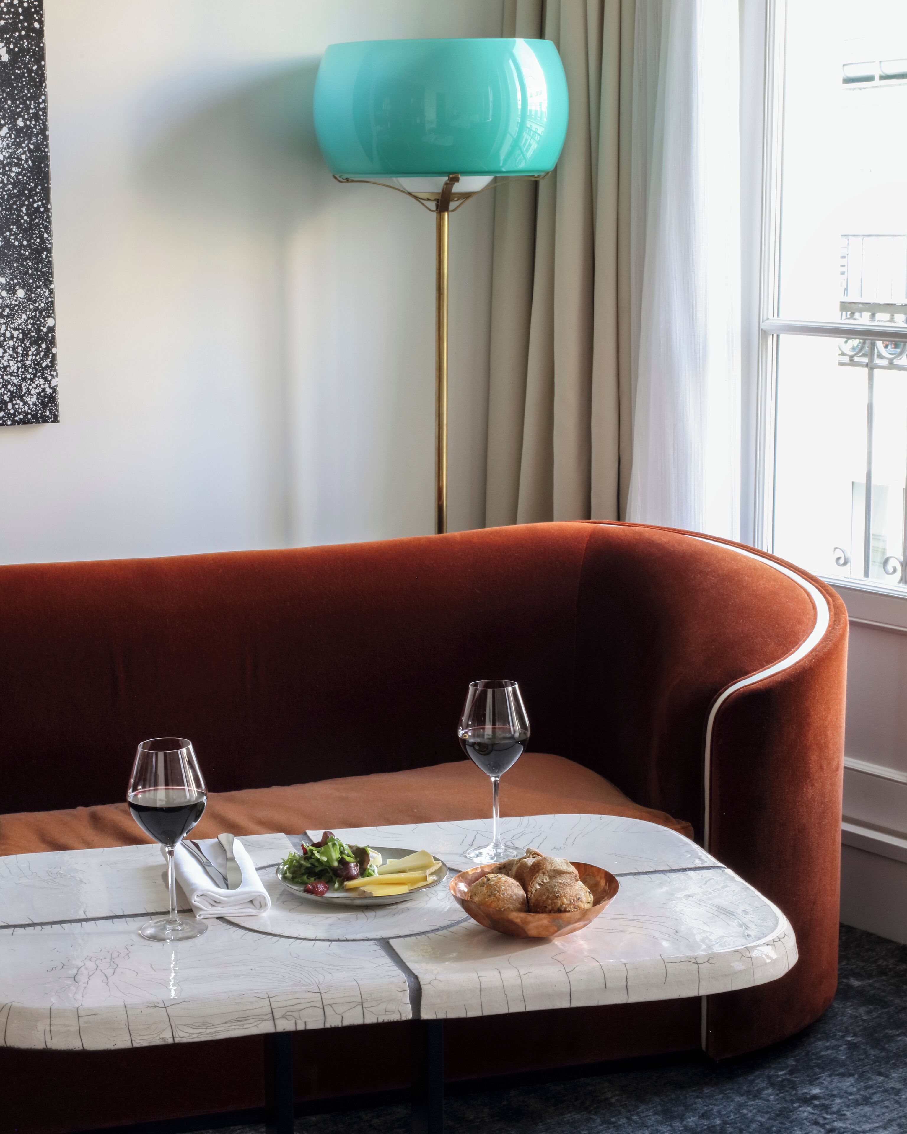 A cozy room with a curved sofa, a small round table with a white marble top, two wine glasses, a plate of cheese and grapes, and a bowl of bread.