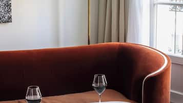 A cozy room with a curved sofa, a small round table with a white marble top, two wine glasses, a plate of cheese and grapes, and a bowl of bread.