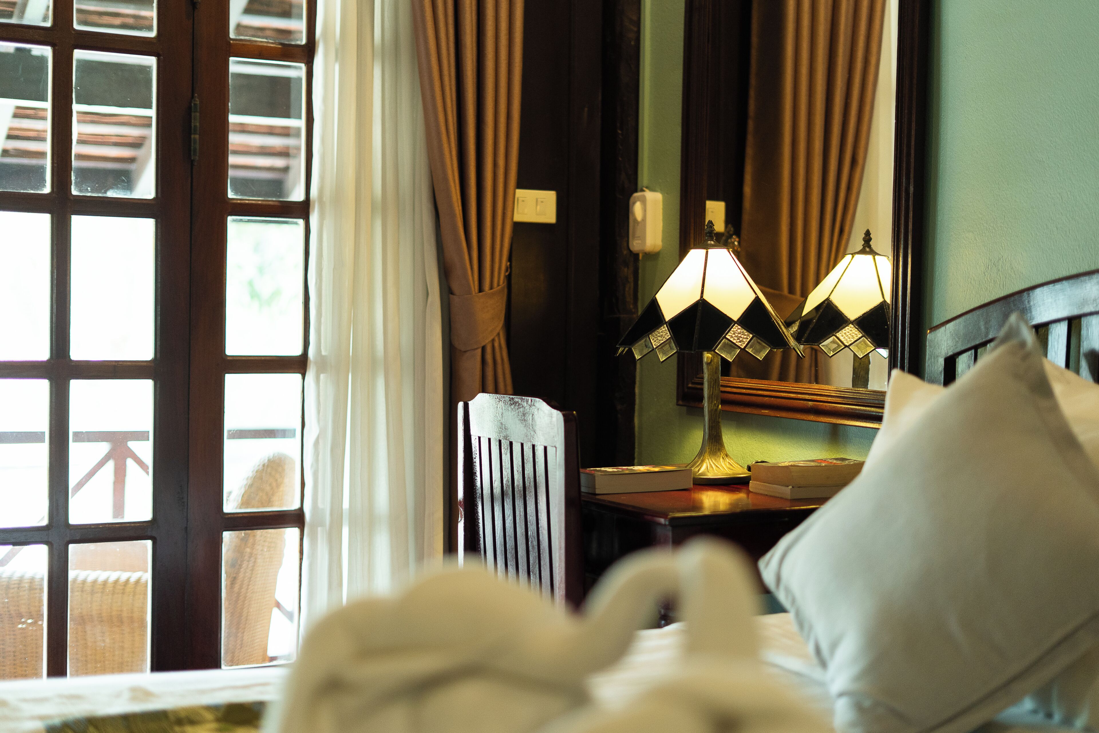 Una habitación de hotel con una cama, una mesita de noche con lámpara, una silla y una ventana con cortinas.