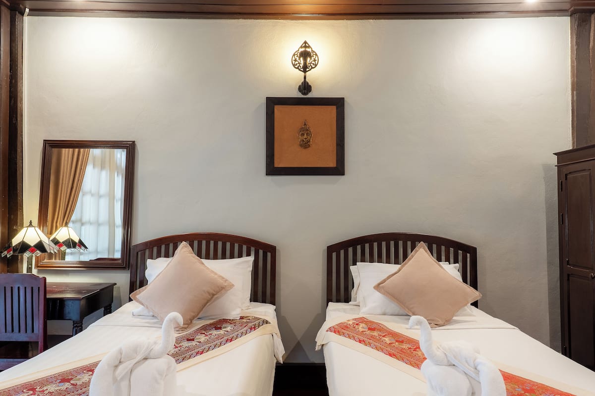 A hotel room with two beds, a desk, a chair, a lamp, and a framed picture on the wall.