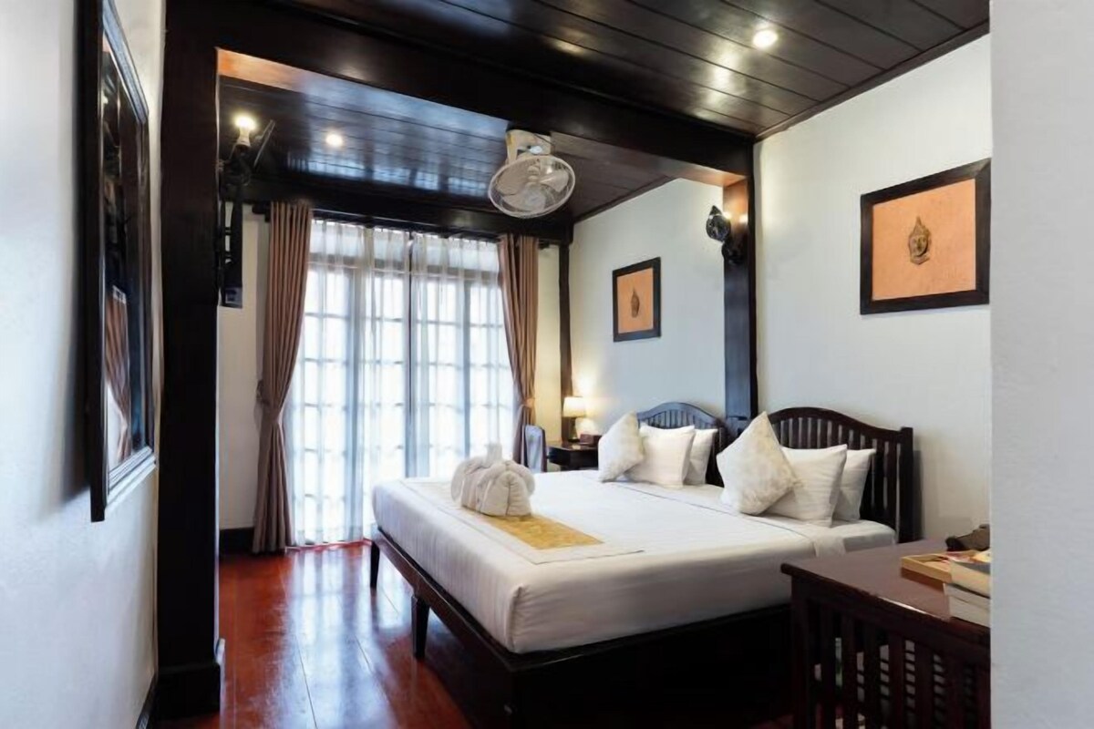 Habitación de hotel con cama, mesita de noche, lámpara y vista al exterior por la ventana.