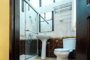 Un baño con cabina de ducha de vidrio, lavamanos pedestal y retrete.